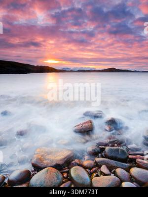 Farbenfroher bewölkter Himmel bei Sonnenaufgang an einem felsigen Strand. Bei Reiff an der Westküste Schottlands Stockfoto