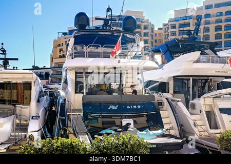 St. Julian's, Malta - 3. November 2025: Eine freischaffende Frau, die auf einem luxuriösen Yachtdeck mit moderner Architektur im Hintergrund an ihrem Laptop arbeitet. Stockfoto