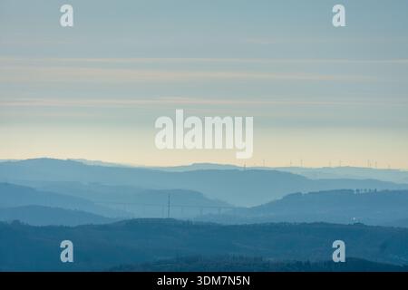 Sanfte blaue Hügelschichten und weit entfernte Bergrücken verblassen unter einem ruhigen Himmel in atmosphärischen Dunst. Stockfoto