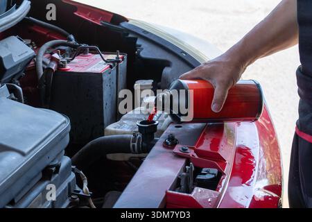 Nahaufnahme einer Hand, die rotes Kühlmittel in das Kühlersystem eines Fahrzeugs gießt. Fahrzeugwartung, Reparatur von Heimwerkerfahrzeugen, Motorkühlung, Autoservice Stockfoto