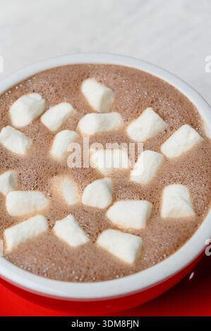 Heiße Schokolade mit weißen Marshmallows in einem roten Keramikbecher. Eine Tasse heißer Kakao mit weißen Marshmallows zum Nachtisch in einem Café, Nahaufnahme Stockfoto