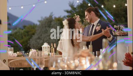 Tanzende Braut und Bräutigam halten Hände auf der Terrasse in der Abenddämmerung, tragen Kleid Schleier Marineblau Boutonniere Stockfoto