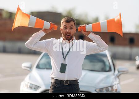 Spaß mit den Kegeln haben, ihnen zuhören. Fahrschularbeiter ist draußen in der Nähe des Autos. Stockfoto