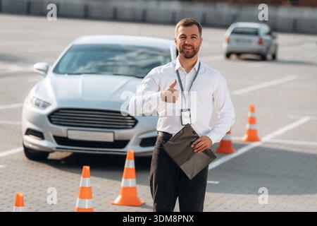 Daumen hoch Geste, lächelnd. Fahrschularbeiter ist draußen in der Nähe des Autos. Stockfoto