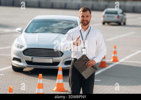 Daumen hoch Geste, lächelnd. Fahrschularbeiter ist draußen in der Nähe des Autos. Stockfoto