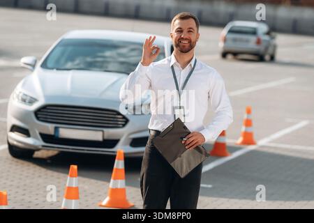 Notizblock ist in der Hand. Fahrschularbeiter ist draußen in der Nähe des Autos. Stockfoto