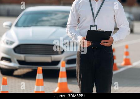 Notizblock liegt in der Hand. Fahrschularbeiter ist draußen in der Nähe des Autos. Stockfoto