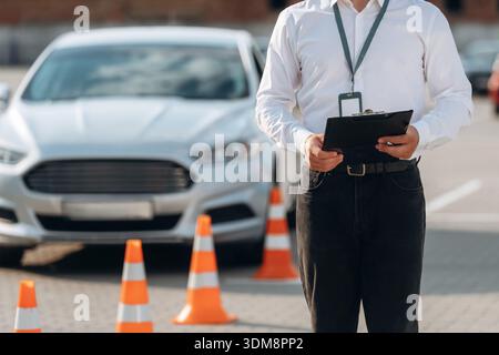 Notizblock liegt in der Hand. Fahrschularbeiter ist draußen in der Nähe des Autos. Stockfoto