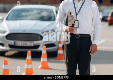 Notizblock liegt in der Hand. Fahrschularbeiter ist draußen in der Nähe des Autos. Stockfoto