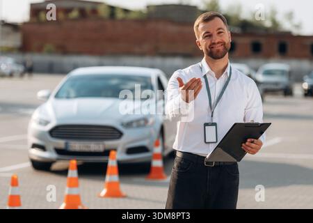 Begrüßungsgeste. Fahrschularbeiter ist draußen in der Nähe des Autos. Stockfoto