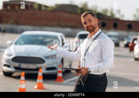 Begrüßungsgeste. Fahrschularbeiter ist draußen in der Nähe des Autos. Stockfoto