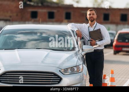 Sich auf das Auto zu lehnen. Fahrschularbeiter ist draußen. Stockfoto