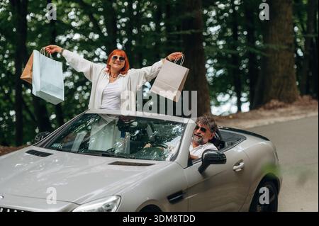 Papiereinkaufstaschen in den Händen der Frau. Seniorenpaar, das Cabriolet fährt. Stockfoto