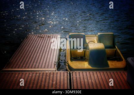 Ein ruhiges Tretboot ruht an einem sonnendurchfluteten Holzsteg Stockfoto