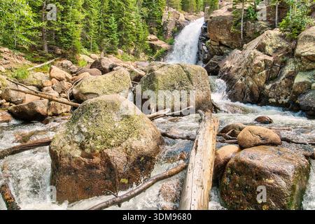 Ein Wasserstrom fließt über ein felsiges Flussbett. Die Felsen sind groß und zerklüftet und das Wasser ist kristallklar. Die Szene ist friedlich und ruhig, mit Stockfoto