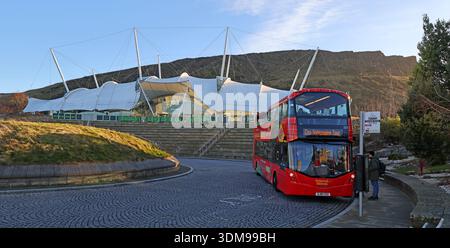 Roter Sightseeing-Bus mit offenem Oberdeck vor dem Dynamic Earth Science Centre und dem Planetarium auf der Holyrood Road, mit Salisbury Crags und Holyrood Park im Winter Stockfoto