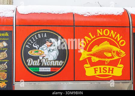 CELJE, SLOWENIEN, 01.03.2026: Leuchtend rote Food Truck-Schilder mit dem Dal Nonno Pizzeria-Logo und einem kräftigen gelben Fisch, mit Schnee auf dem Dach, showca Stockfoto