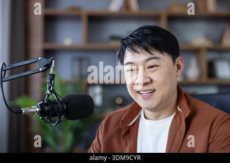 Ein Mann, der aktiv mit einem Mikrofon interagiert, Audioinhalte für einen Podcast oder eine Übertragung aus einem modernen Heimstudio erstellt und seine Botschaft an ein Publikum weitergibt Stockfoto