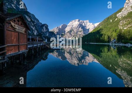 Der Berg Seekofel spiegelt sich im Pragser See. Ein hölzernes Bootshaus steht über dem klaren Wasser mit steilen Berghängen in der Ferne. Stockfoto