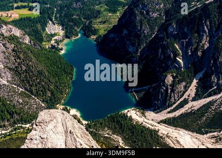Aus der Vogelperspektive auf den Pragser See. Tiefblauer See umgeben von steilen Berghängen und grünen Wäldern in der Ferne. Stockfoto