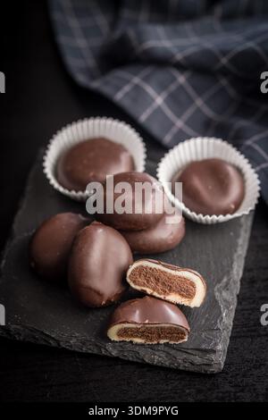 Dunkle Schokoladentrüffel in Form von Kaffeebohnen auf einem schwarzen Tisch. Stockfoto