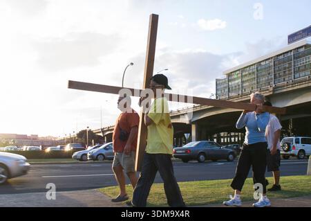 Christen in Waialae – Kahala, Honolulu, trugen 2008 ein großes Holzkreuz entlang einer Stadtstraße, um der Kreuzigung Jesu Christi zu gedenken. Die Prozession zog eine kleine Menge von Anhängern an, die neben dem Kreuzträger spazierten. Diese jährliche Veranstaltung ist eine Demonstration des Glaubens und der religiösen Einhaltung für die örtliche christliche Gemeinschaft. Stockfoto