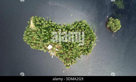 Von oben nach unten auf eine kleine bewaldete Insel, umgeben von einem ruhigen Süßwassersee im ländlichen Schweden, mit dichten borealen Bäumen, dunklem Wasser, abgelegen Stockfoto