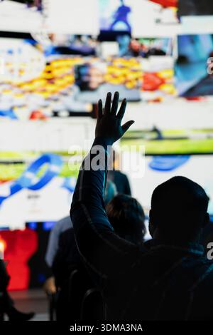 Selektiver Fokus des Schwarzen Mannes, der die Hand erhebt, um Fragen bei Social Media-Präsentationen zu stellen, und während des Panels der Branding-Konferenz eine Diskussion mit dem Moderator führt. Junger Erwachsener auf dem Business Summit. Stockfoto