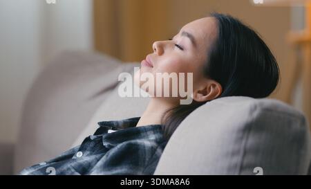 Seitenansicht ruhig entspannte asiatische Koreanerin ruht mit geschlossenen Augen auf Sofa zu Hause japanische Frau liegend auf Couch träumend schlafen faule Zeit Komfort Stockfoto