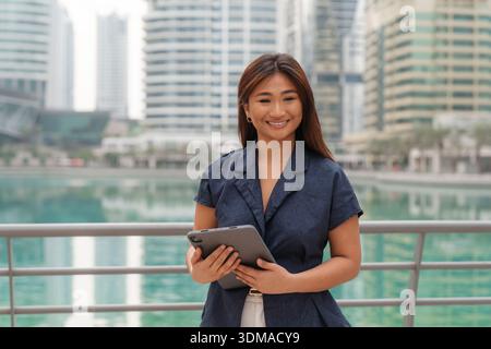 Porträt einer schönen, lächelnden, selbstbewussten asiatischen Geschäftsfrau, die ein Tablet verwendet und in der städtischen Umgebung steht. Stockfoto