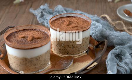 Zwei köstliche Tiramisu-Haferflocken in klaren Glasbehältern, mit cremigem Haferflocken, Kaffee und Kakaopulver, garniert mit Schokoladenstückchen und Stockfoto