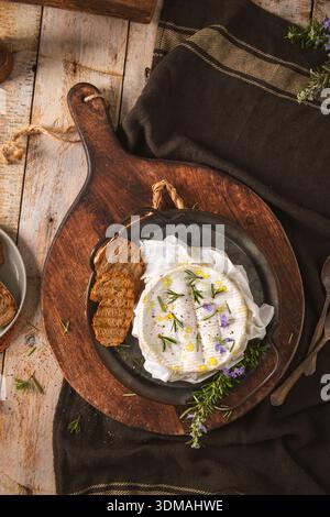 Ein Blick von oben auf geschmolzenen Camembertkäse, garniert mit frischem Rosmarin und Olivenöl. Die warme, rustikale Ästhetik ist mit dunkler Bettwäsche und knusprigem bre ausgestattet Stockfoto
