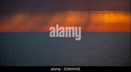 Am Lake Superior fällt Regen aus, während der Himmel orange leuchtet, kurz bevor die Sonne über dem Horizont aufgeht. Stockfoto