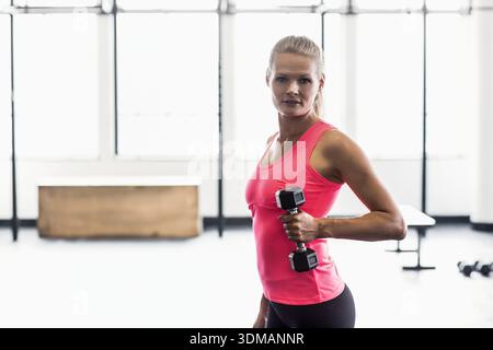 Weiblich in leuchtend rosa Top und schwarzen Leggings heben Hex Hantel im Fitness Studio, Kopierraum. Frau, Fitnessstudio, Gewichte, Training, Kraft, minimalistisch, Stockfoto