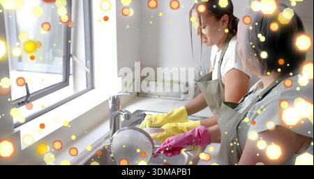 Zwei Frauen in Schürzen waschen Geschirr im Spülbecken, mit Metallsieb, gelben, rosa Handschuhen Stockfoto