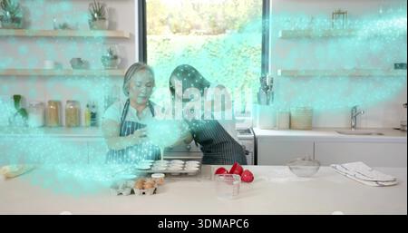 Teig gießen, Mutter und Teenager machen Cupcakes in der Küche in gestreiften Schürzen mit Schüssel Stockfoto