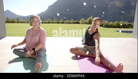 Eine ältere Frau und eine Teenager-Tochter, die sich auf der Terrasse dehnen, Trainingskleidung auf Matten tragen Stockfoto
