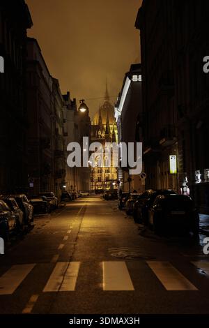 Budapest, Ungarn, Ungarn. Februar 2026. Das ungarische Parlamentsgebäude wird bei Nacht beleuchtet und durch Gebäude auf einer Straße in Budapest gesehen. (Kreditbild: © Bianca Otero/ZUMA Press Wire) NUR REDAKTIONELLE VERWENDUNG! Nicht für kommerzielle ZWECKE! Stockfoto