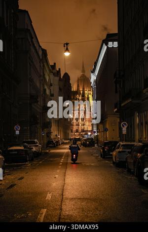 Budapest, Ungarn, Ungarn. Februar 2026. Das ungarische Parlamentsgebäude wird bei Nacht beleuchtet und durch Gebäude auf einer Straße in Budapest gesehen. (Kreditbild: © Bianca Otero/ZUMA Press Wire) NUR REDAKTIONELLE VERWENDUNG! Nicht für kommerzielle ZWECKE! Stockfoto