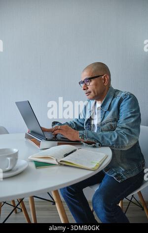 Mann, der auf einem Laptop mit offenem Notebook und Kaffeetasse auf einem weißen Schreibtisch tippt Stockfoto