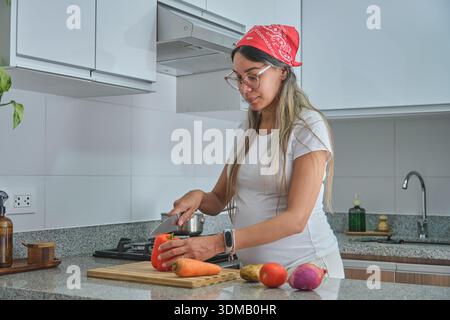 Schwangere Frau, die frisches Gemüse auf einem Schneidebrett schneidet, um eine gesunde Ernährung zu fördern Stockfoto