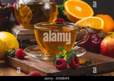 Tee in einem Glasbecher auf dem Tisch neben Minze, Himbeeren und Früchten Stockfoto
