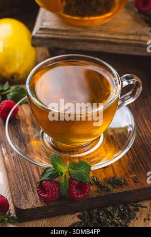 Tee in einem Glasbecher auf dem Tisch neben Minze, Himbeeren und Früchten Stockfoto