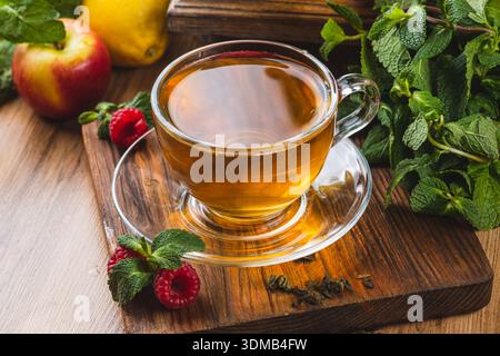 Tee in einem Glasbecher auf dem Tisch neben Minze, Himbeeren und Früchten Stockfoto