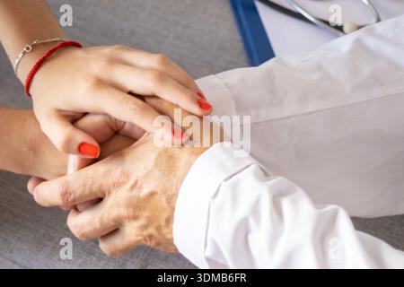 Die Hände des Arztes trösten die Hand eines Patienten auf grauem Hintergrund. Konzept von Vertrauen, Unterstützung, Betreuung und Empathie in der Medizin Stockfoto