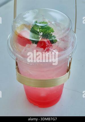 Eine leuchtend rosa Eissoda, garniert mit einer Zitronenscheibe, Maraschino-Kirschen und Petersilie, präsentiert in einem klaren Plastikbecher auf hellem Hintergrund, Perf Stockfoto