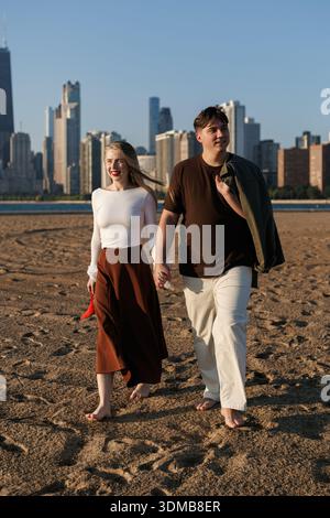 Reifes kaukasisches Paar, das am Strand läuft und Hände hält. Dateitag des modischen Mannes und der modischen Frau Stockfoto