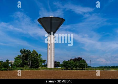 Moderner Betonwasserturm, der über einem ländlichen Feld ragt und grüne Bäume unter einem blauen Himmel mit schimmernden Wolken. Stockfoto