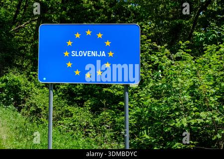 Blaues Grenzschild der Europäischen Union für Slowenien mit gelben Sternen vor grünen Blättern und Bäumen. Stockfoto
