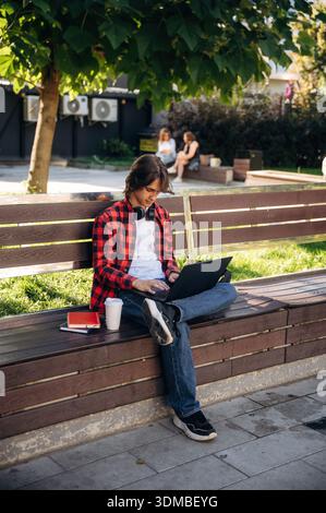 Der Laptop liegt auf den Beinen. Der Student ist im öffentlichen Park draußen. Stockfoto